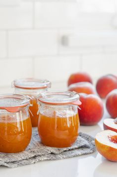 several jars filled with liquid sitting on top of a table next to sliced peaches