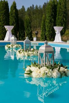 an outdoor swimming pool decorated with white flowers and greenery for a wedding ceremony or reception