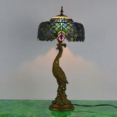 a lamp with a peacock on it sitting on top of a green table next to a white wall