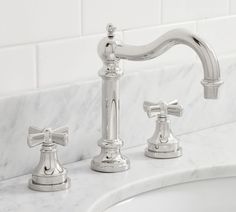 two chrome faucets sitting on top of a white marble counter next to a sink