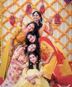 four women pose for a photo in front of a backdrop with hanging bells and decorations