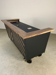 a black and wood desk with wheels on the bottom is sitting in a white room