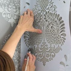 a woman is using a stencil to decorate a wall