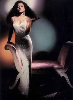 a woman in a white dress standing next to a pink chair with her hand on her hip