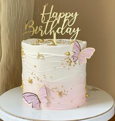 a pink and white cake with gold butterflies on it's top is sitting on a table