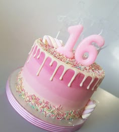 a pink birthday cake with sprinkles and the number six on it's top