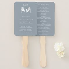 two wooden spatulas with wedding programs on them next to a white and blue flower