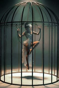 a woman is in a cage with a hoop around her neck and legs as she stands on one leg