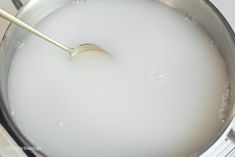 a metal pan filled with milk on top of a stove burner and a spoon sticking out of it