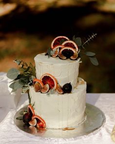 a three tiered cake with figs and greenery on the top is decorated with fresh fruit