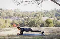 a woman doing push ups on a mat in the middle of a field with trees