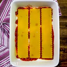 lasagna with sauce and cheese in a white dish on a purple striped towel