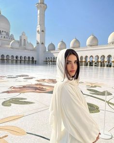 a woman standing in front of a white building with many arches and domes on it