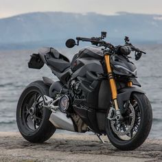 a black motorcycle parked on top of a rock next to the ocean