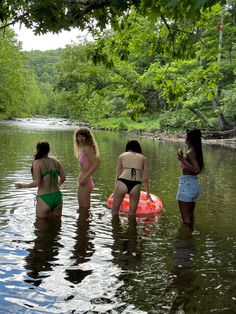 three women in bikinis are standing in the water near an orange raft and some trees