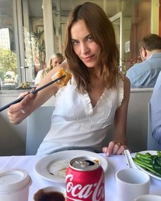 a woman sitting at a table eating food with chopsticks in front of her