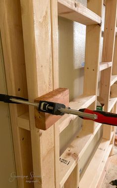 a pair of pliers are hooked up to the side of a wooden shelf that is being built