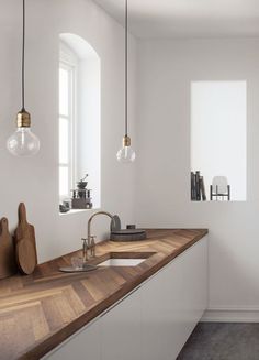 a white kitchen with wooden counter tops and hanging lights above the sink, in front of a window