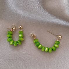 two pairs of green beaded earrings sitting on top of a white cloth covered surface