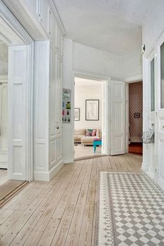 an open door leading to a living room with white walls and wood floors, along with a patterned rug on the floor