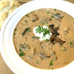 a bowl of mushroom soup with sour cream and parsley on top, next to a piece of bread