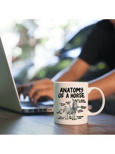 a white coffee mug sitting on top of a wooden table next to a laptop computer