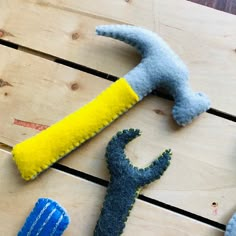 three felt toys are laying on a wooden table together, one is blue and the other is yellow