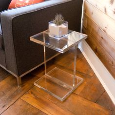 a glass table with a plant on it in front of a couch and wooden floor