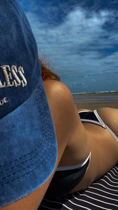 a woman laying on top of a beach next to the ocean wearing a blue hat