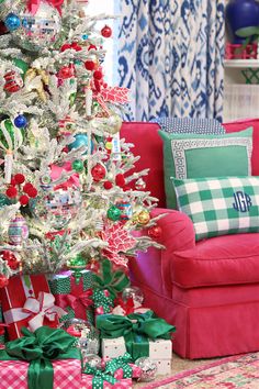 a christmas tree with presents under it in front of a red couch and blue curtains