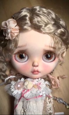 a close up of a doll with blonde hair and big eyes, wearing a white dress