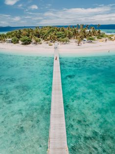 a long pier leading to an island with palm trees in the water and people walking on it