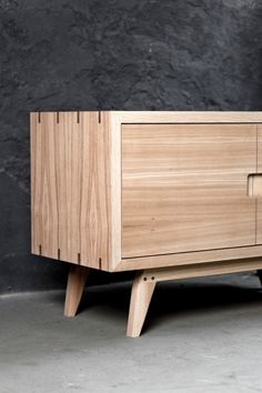 a wooden cabinet sitting on top of a floor next to a black wall with a plant in it