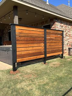 a large wooden fence in front of a brick house with an outdoor hot tub and grill