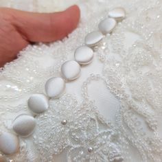 a close up of a person's hand holding buttons on a white wedding dress