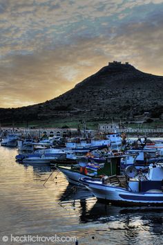 several boats are docked in the water near a hill and some hills with houses on it