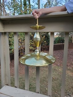 a person holding an oil lamp on top of a wooden porch railing with grass and trees in the background