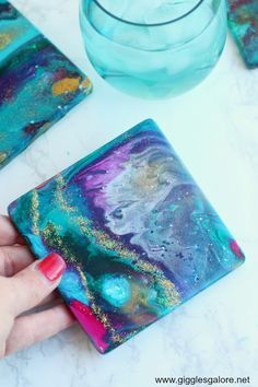 a hand holding a coaster that is painted with acrylic paint