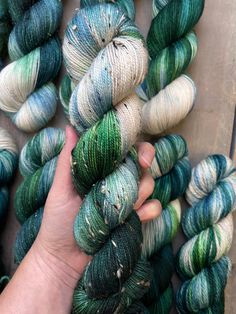 a hand is holding several skeins of yarn in green and white colors on a wooden surface