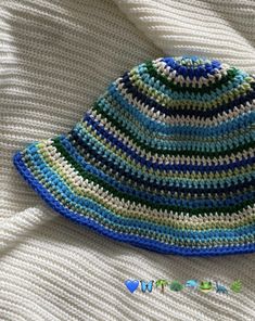 a crocheted blue and green hat laying on top of a white blanket,