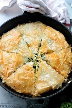 a pie in a cast iron skillet with spinach toppings on the side