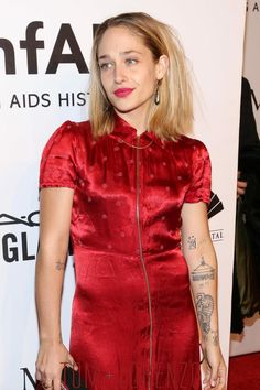 a woman in a red dress with tattoos on her arm and shoulder, standing at an event