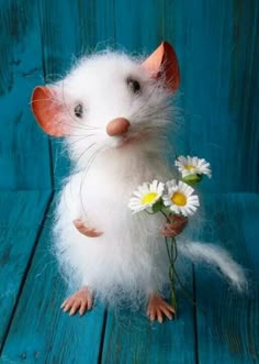 a small white rat sitting on top of a wooden table with daisies in it's paws