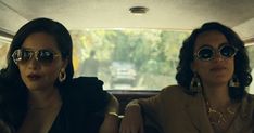 two women sitting in the back seat of a car wearing sunglasses and gold necklaces