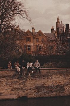 four people sitting on a brick wall next to a body of water with buildings in the background