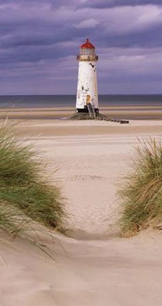 a light house sitting on top of a sandy beach next to the ocean under a cloudy sky