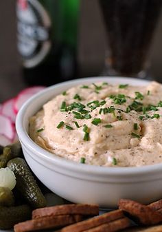 a white bowl filled with dip surrounded by crackers and pretzels