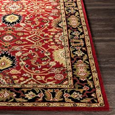 a red rug with black and gold designs on the bottom is laying on a wooden floor