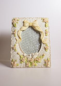 a decorative mirror with a bow on the top and flowers around it's edge