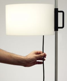 a hand is plugged in to a lamp with a black cord and white shade